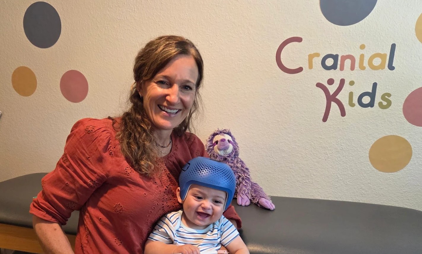 Kristen Thessing smiling with a baby wearing a cranial remolding helmet
